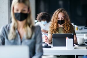 mulheres trabalhando em escritório de máscara em alusão à redução da jornada de trabalho