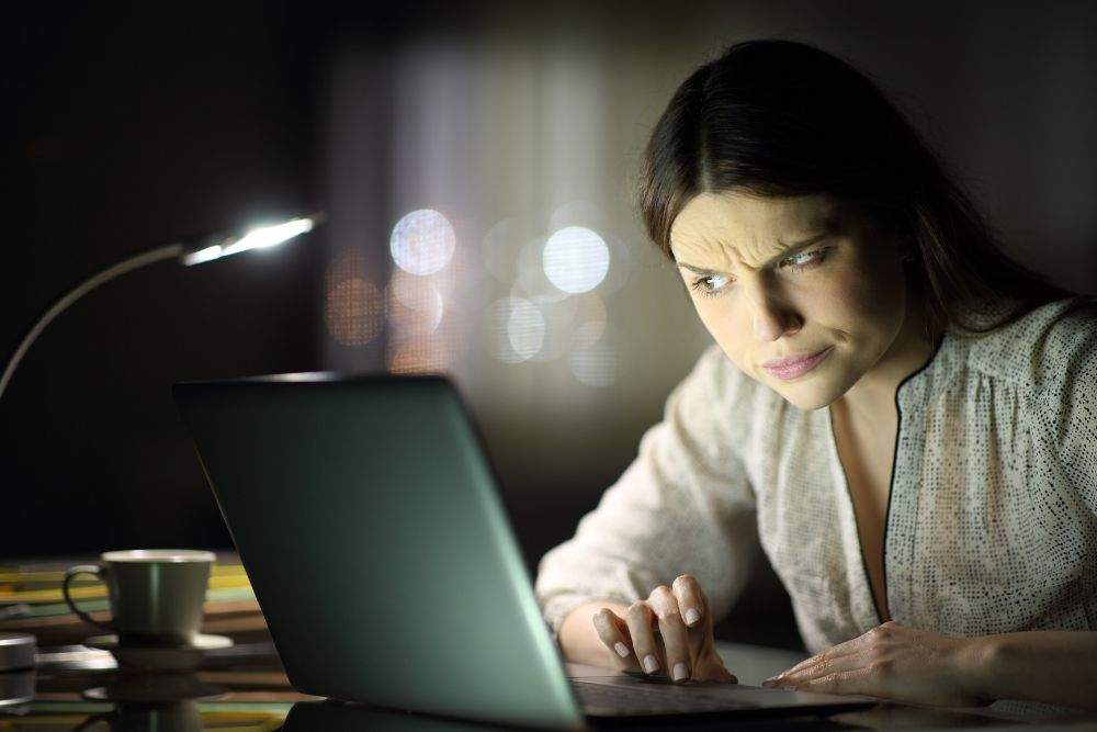 mulher olha para a tela do computador e desconfia de falsa vaga de emprego