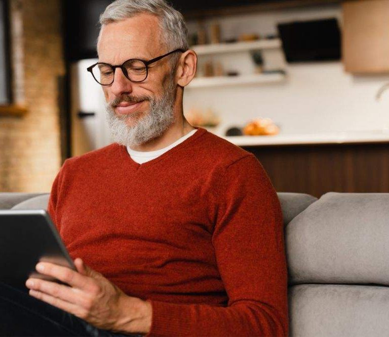 homem está lendo uma das newslettes para gestores em um tablet sentado ao sofá e expressãndo satisfação