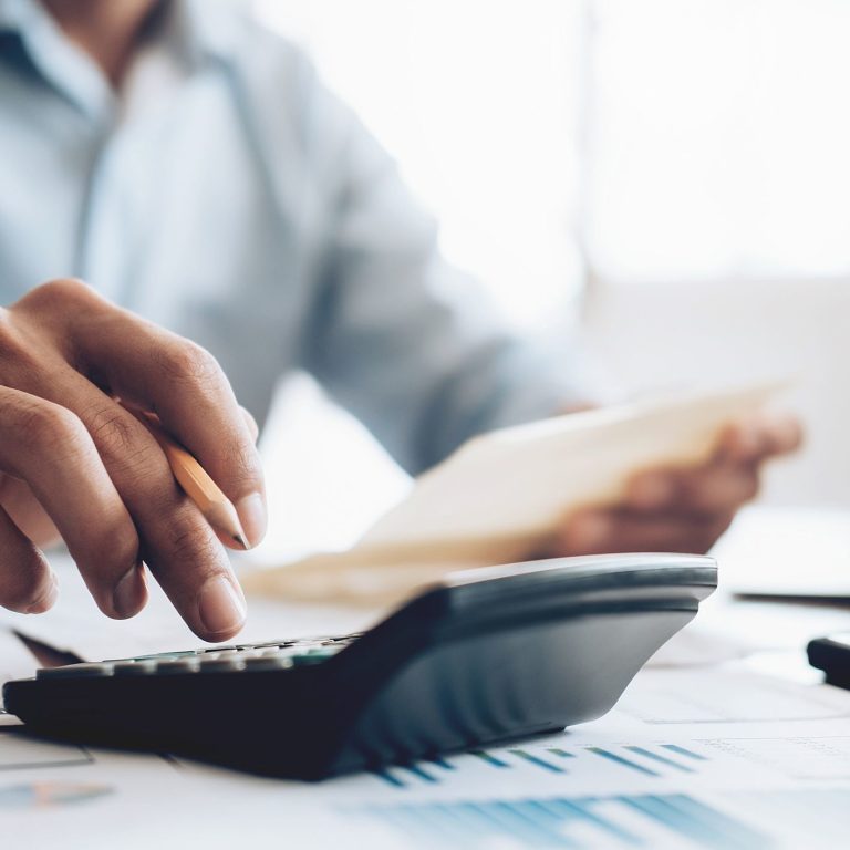 Homem utiliza calculadora e faz anotações para demonstrar como a redução de custos desempenha um papel crucial na gestão e no sucesso de qualquer organização.