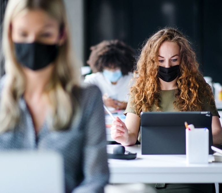 mulheres trabalhando em escritório de máscara em alusão à redução da jornada de trabalho